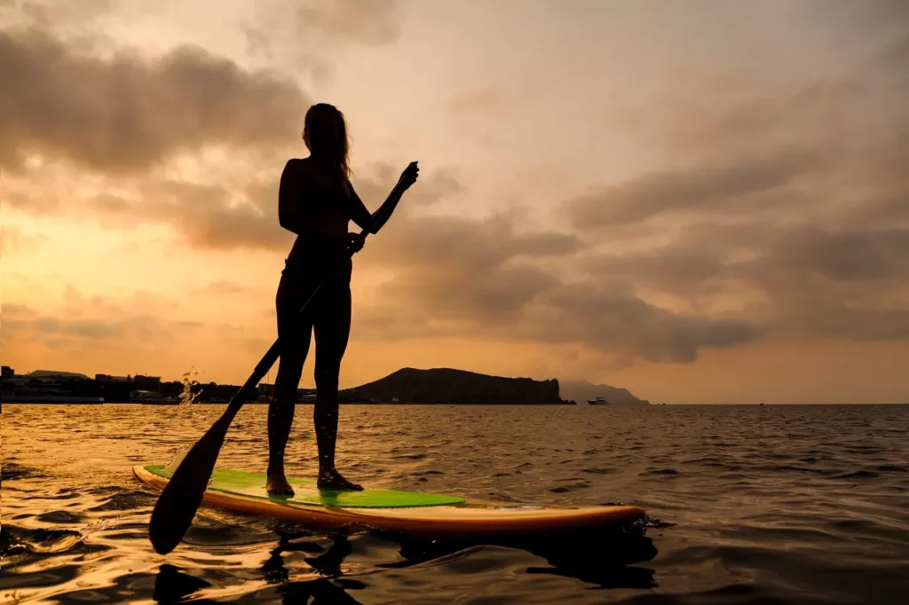 a woman paddle boarding in the ocean at sunset.